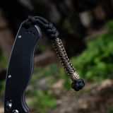 M-Tac Knife Lanyard Scandinavian med flettet paracordstil på lommeknivens skaft i naturlig skovbaggrund