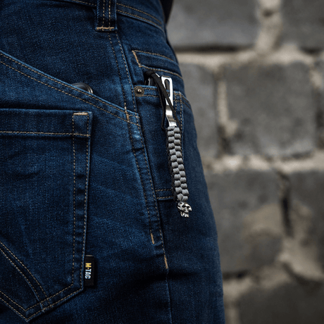 M-Tac Knife Lanyard Cuboid Skull med dekorativ perle, der hænger fra en knivlomme i blå jeans
