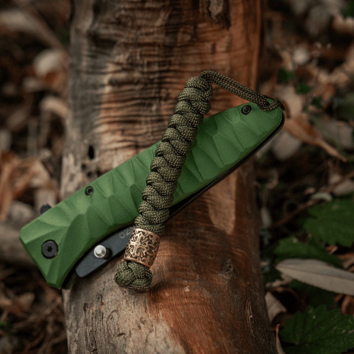 M-Tac Viper Lanyard Scandinavian i flettet paracord design med Viper-perle, placeret på en grøn lommekniv på en træstamme