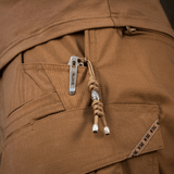 M-Tac Zeus Stainless Steel Lanyard i lommen på brune bukser med dekorativ perle og flettet paracord, nem adgang til kniv eller udstyr.