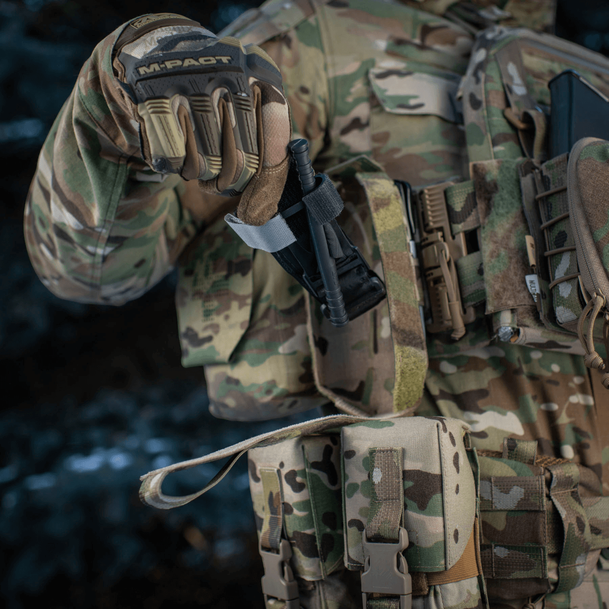 Militærpersonel holder M-Tac Lomme til Tourniquet Closed på taktisk vest, klar til nødsituationer.