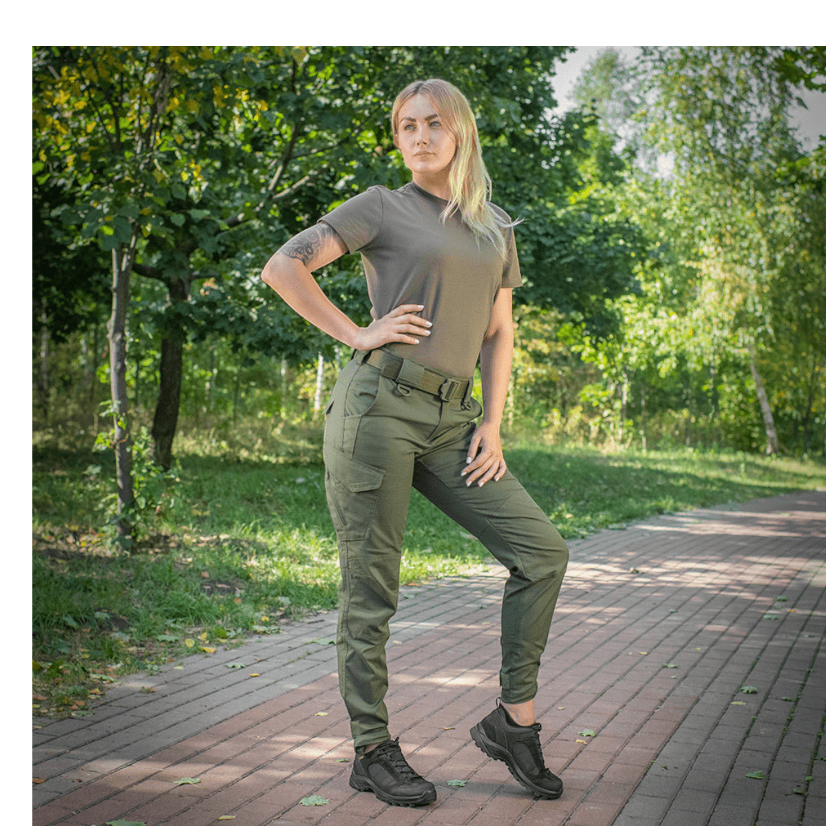 Kvinde iført M-Tac Bukser Aggressor Dame Flex på en sti i parken, ideel til træning og udendørs aktiviteter, fremhæver fleksibilitet og stil.