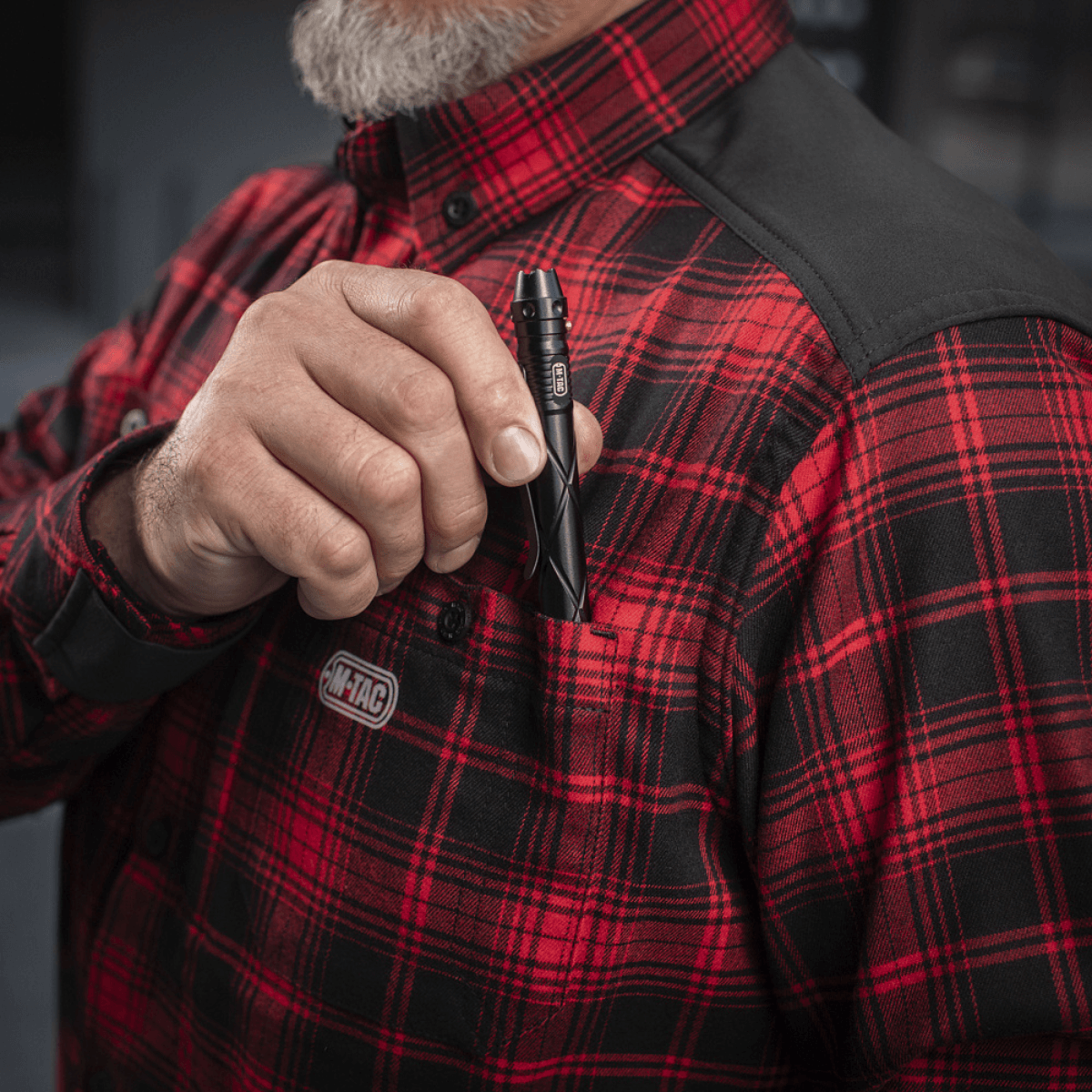 Person iført M-Tac Redneck Skjorte i rød plaidmønster med en lommepen i brug. Fremhævet for styrke og komfort.