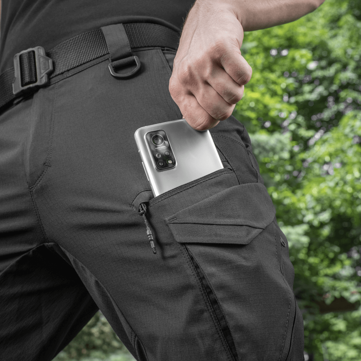 Mand iført M-Tac Aggressor Summer Flex Shorts med telefon i sidelomme, fremvist i udendørs omgivelser.