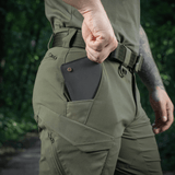 M-Tac Aggressor Summer Flex Shorts i grønt, viser praktisk lomme med smartphone, ideel til udendørs aktiviteter og friluftsliv.