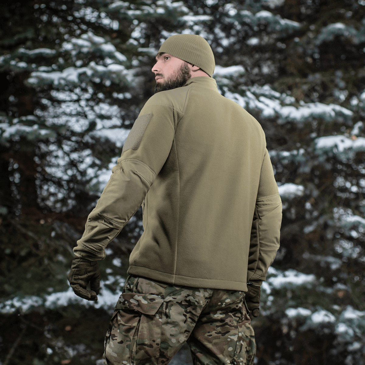 Mand iført M-Tac Combat Fleece Polartec Jakke i skovmiljø med sne på træerne, set bagfra, viser funktionelt design og materialer.