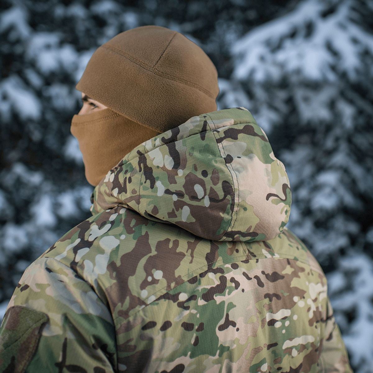 Person i M-Tac Alpha Gen.IV Pro Primaloft Vinterjakke med Multicam mønster, udendørs i snefyldt landskab.