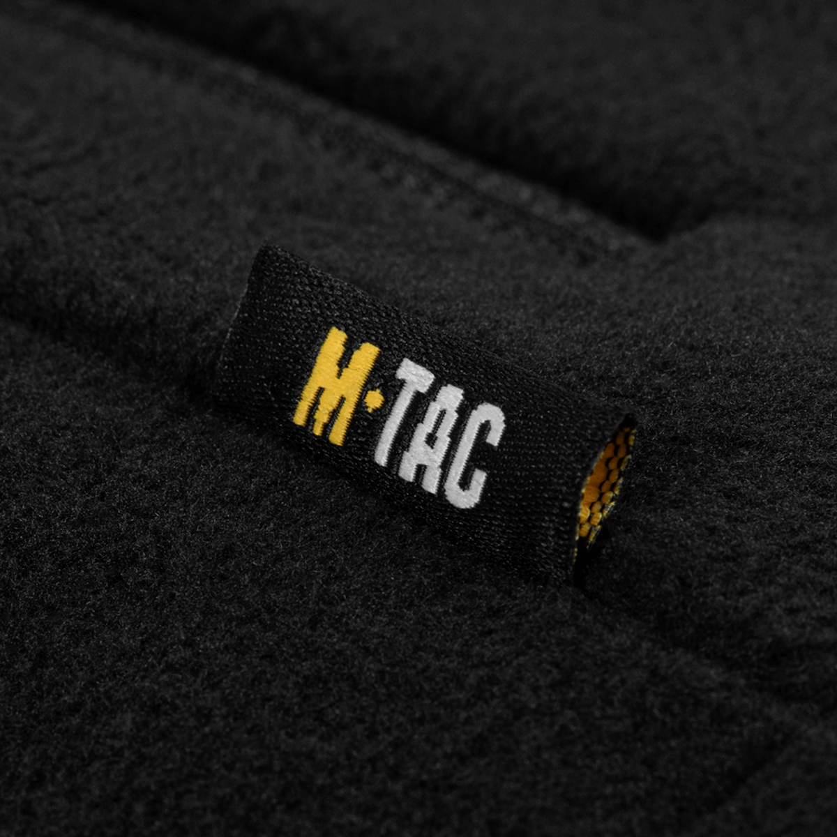 Nærbillede af M-Tac mærke på M-Tac Combat Fleece Jakke Polartec Dame i sort fleece materiale, designet til komfort og høj funktionalitet.
