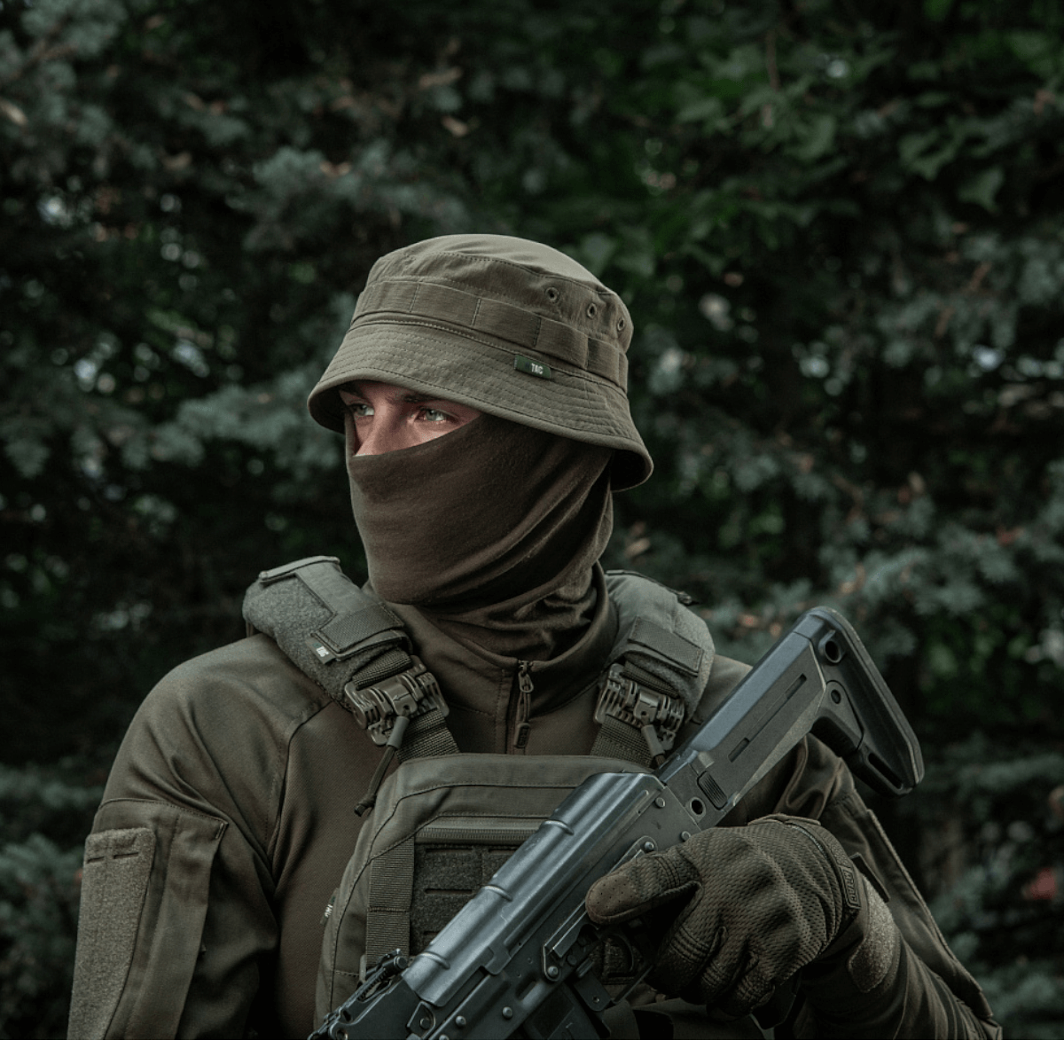 Person wearing tactical gear and hat in outdoor setting