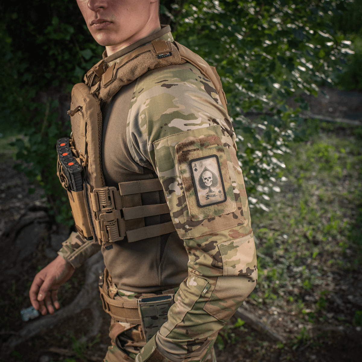 Mand i camouflage med M-Tac Patch Ace of Spades på armen i naturmiljø.