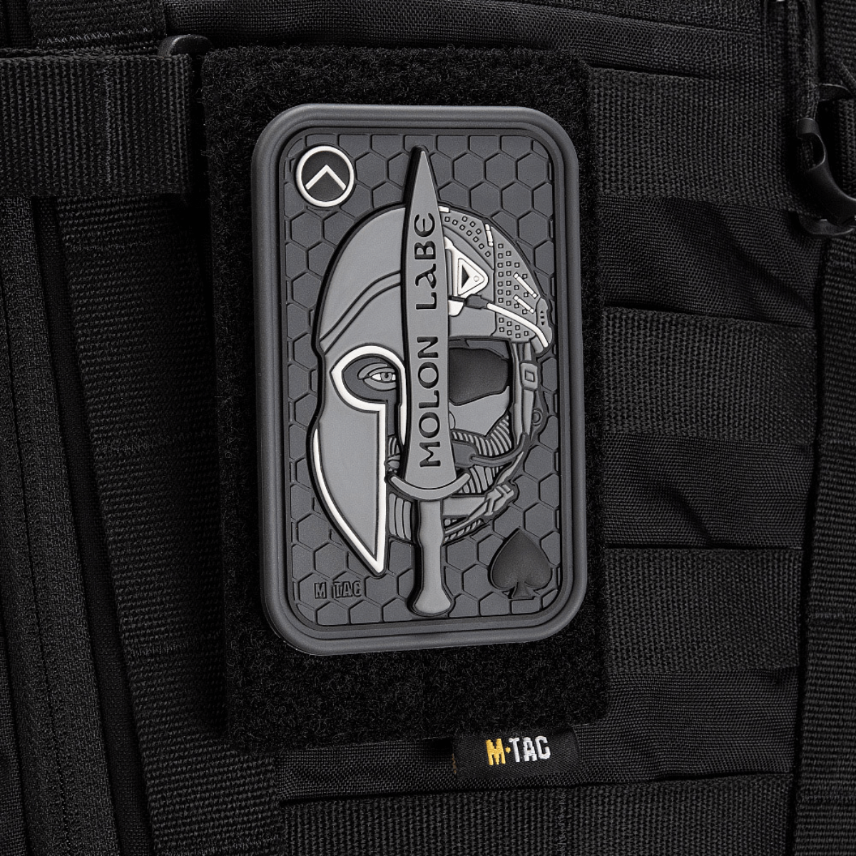 M-Tac Patch Molon Labe 3D PVC med spartansk design og velcro, fastgjort på taktisk taske. Gummi materiale med 3D-effekt. Dimensioner: 108x68 mm.