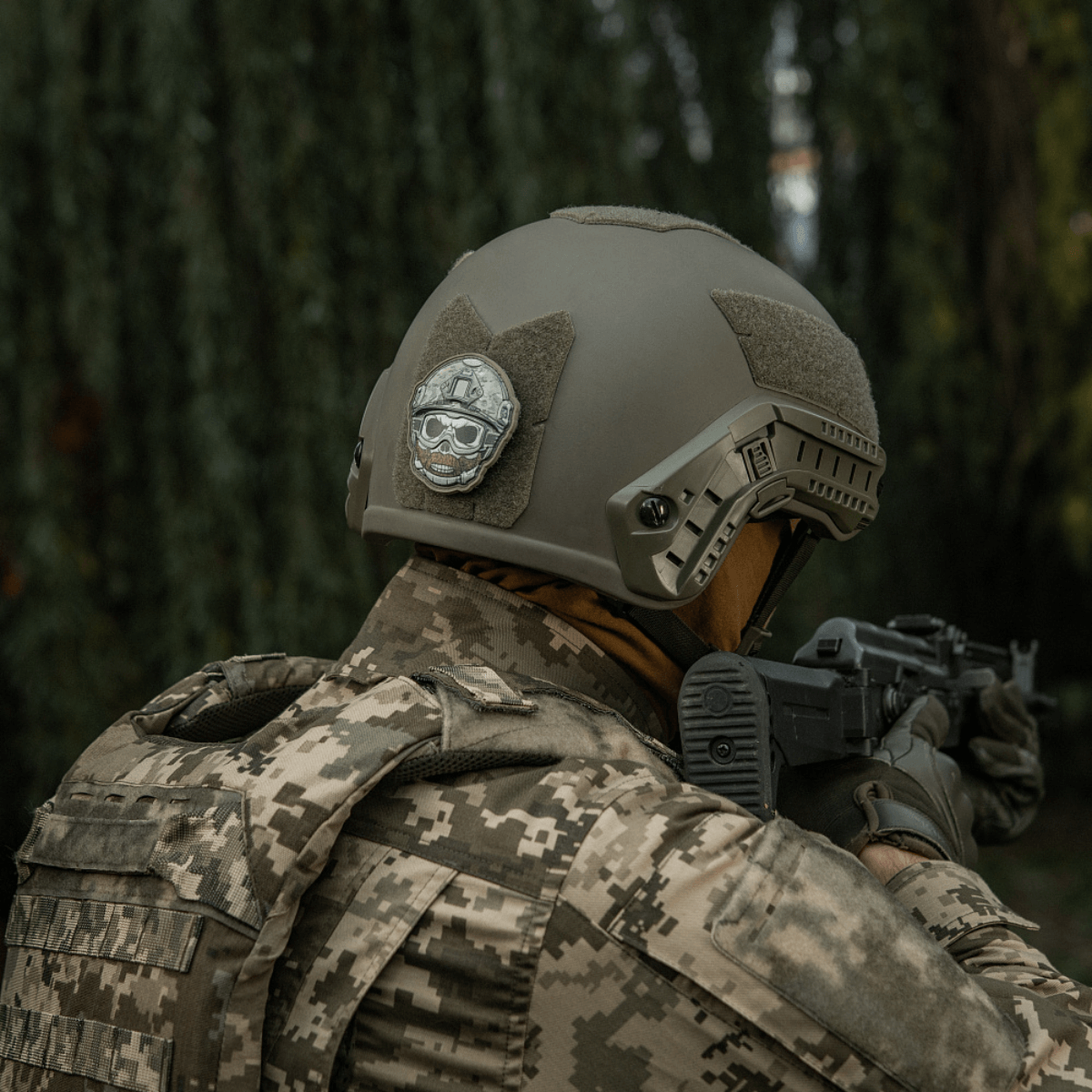 Soldat iført taktisk hjelme med M-Tac Patch Emoji #4 i skoven, PVC med 3D-effekt og Velcro, morale patch, 6.5 x 6.5 cm, holdbar og sjov.