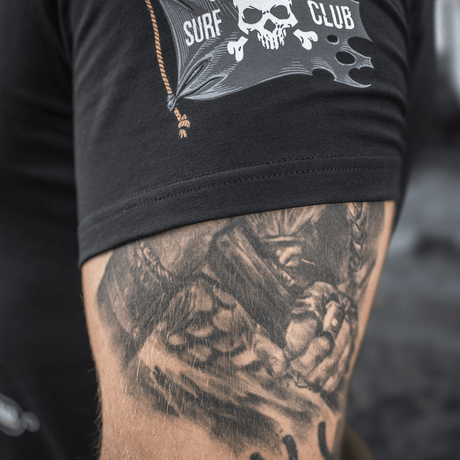 Sort M-Tac T-Shirt Surf Club med en surfkranium printdetalje og tatoveret underarm, designet til at symbolisere styrke og stil.