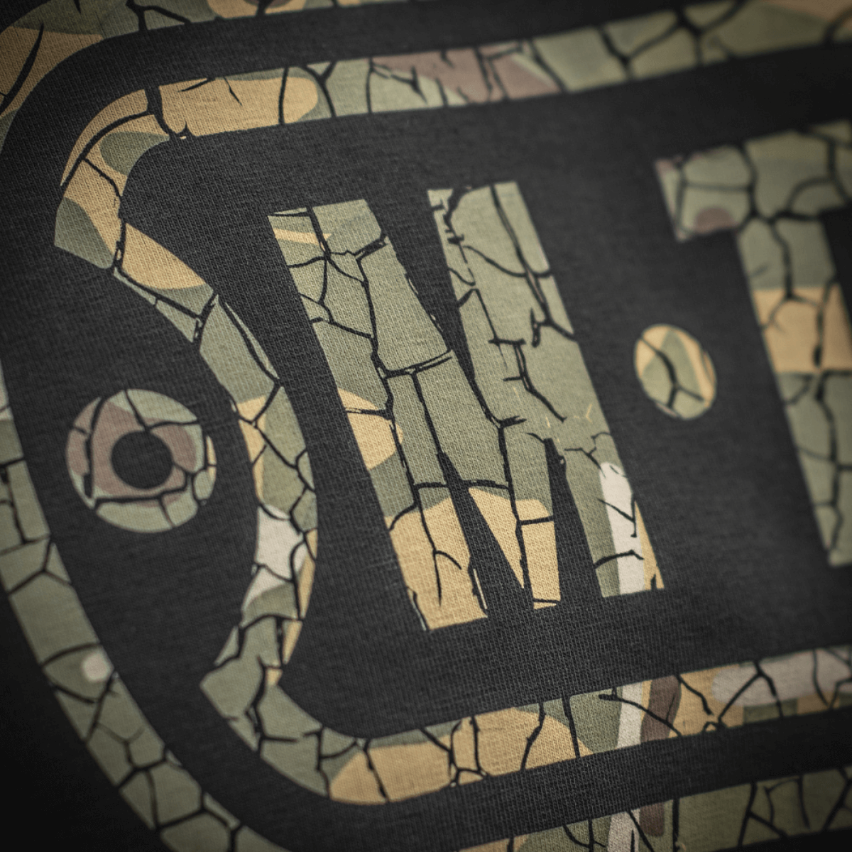 M-Tac T-Shirt Logo med camouflage mønster og ikonisk logo nærbillede, viser stil og kvalitet, slogan på ærme og rygdetaljer.