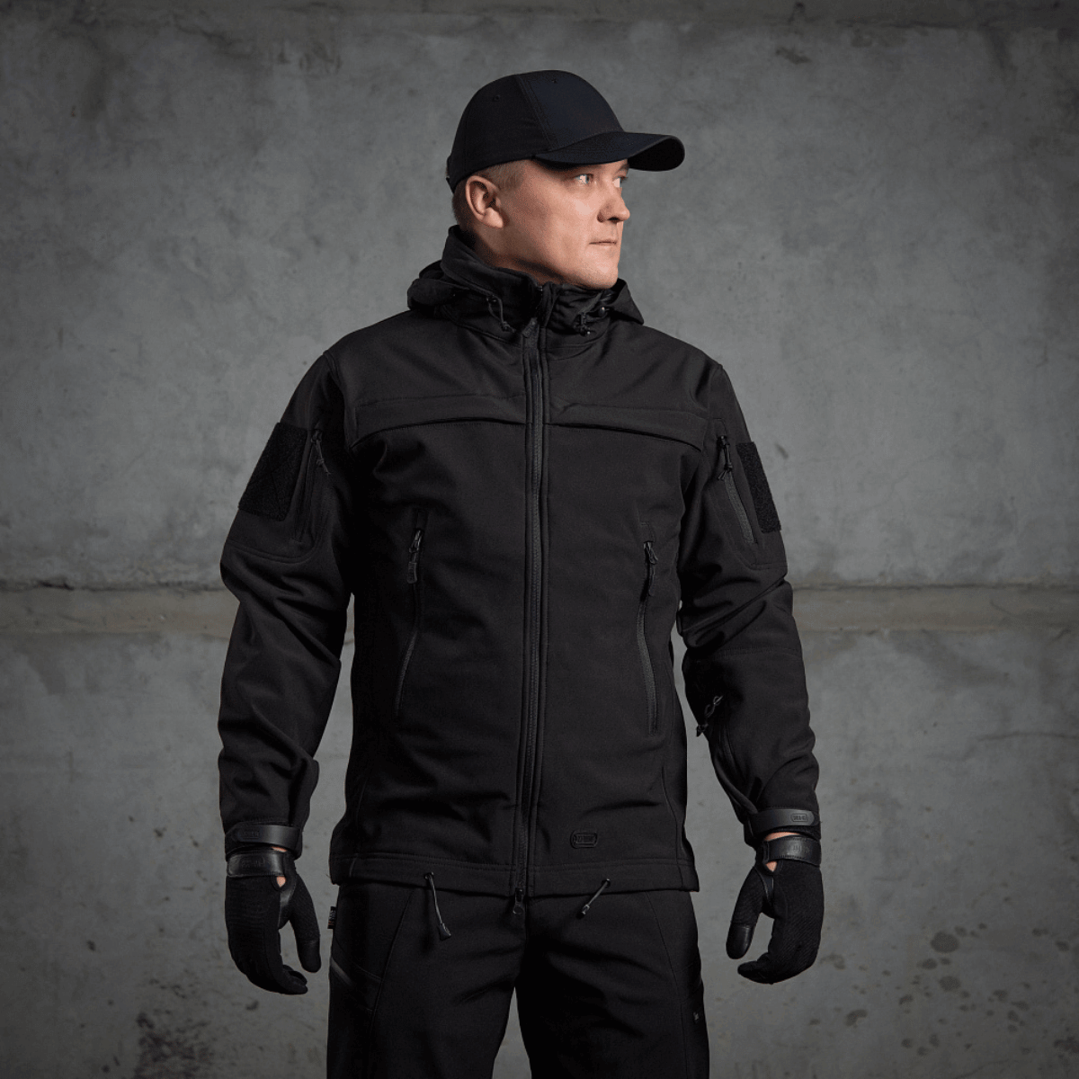 Mand iført M-Tac Soft Shell Police Jakke, sort jakke med justerbare elementer og indvendig fleece, designet til beskyttelse mod vind og vejr.
