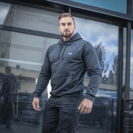 Mand iført M-Tac Hættetrøje Cotton Raglan med komfortabel pasform, egnet til både hverdags- og aktiv livsstil, foran glasbygning.