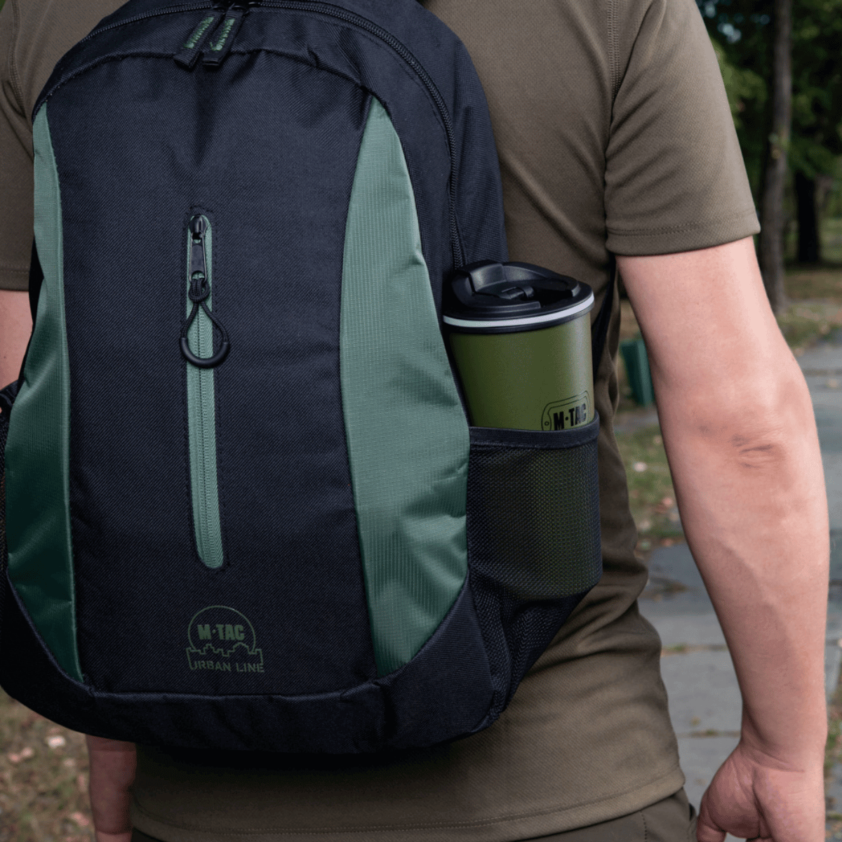 Mand med rygsæk, der indeholder en M-Tac Termokop 450 ml med Ventil, ideel til varme og kolde drikke på farten.
