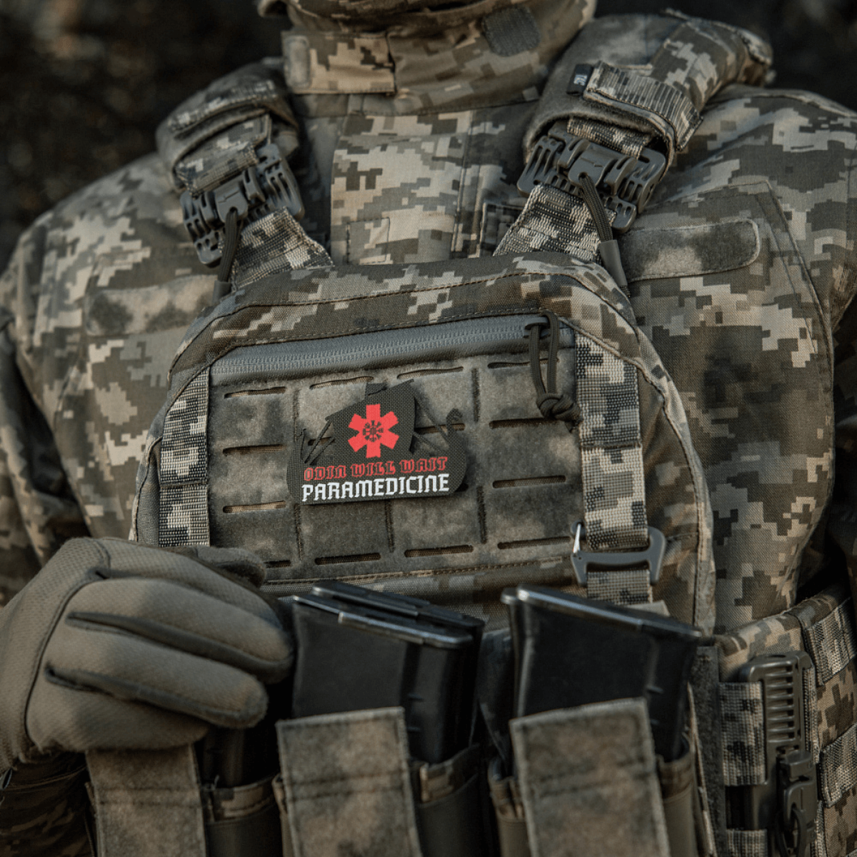 Taktisk vest med påsat patch, "Odin Vils Make Paramedicine", i camouflagemønster.