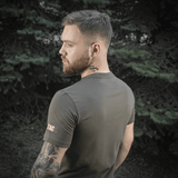 Mand bærer M-Tac Sniper T-shirt i skovmiljø, viser holdbar og komfortabel pasform af 93% bomuld og 7% elastan, ideel til udendørs brug.