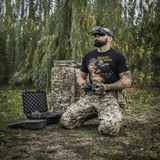 Mand iført M-Tac T-Shirt Delivery Service, inspireret af amerikansk Pin-Up-kultur, styret drone i camouflagetøj i naturen.