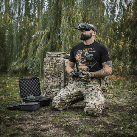 Mand iført M-Tac T-Shirt Delivery Service, inspireret af amerikansk Pin-Up-kultur, styret drone i camouflagetøj i naturen.