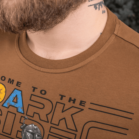 Mand iført brun T-shirt med grafisk print, tæt på visning af halsen og en del af designet.