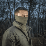 Mand bærer M-Tac Tube Scarf Polartec i skov omgivelser, stilfuldt og varmt halstørklæde til udendørs aktiviteter i kolde årstider.