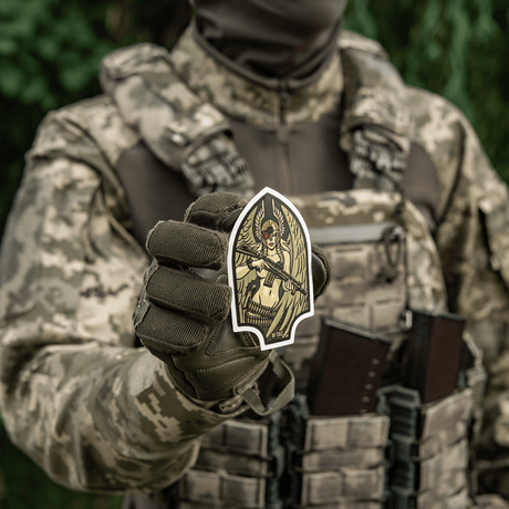 Soldat iført kamouflageuniform, der holder M-Tac Sticker Valkyrie, som viser en krigsgudinde med stiliseret hjelm og M4 gevær.