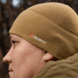 Person iført M-Tac Fleece Watch Cap Light Polartec i sandfarvet fleece, ideel til vinterbrug, fremstillet af Polartec Micro Series materiale.