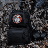 Sort rygsæk med M-Tac Patch Sons of Odin 3D Velcro i skovklædt område, velegnet til taktisk brug og fritid.