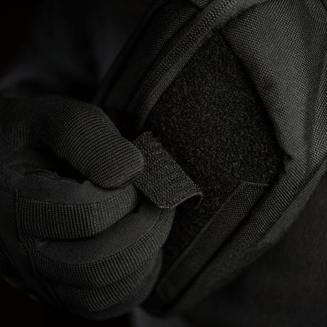 Person iført sort handske justerer M-Tac Patch Valknut Laser Cut Odin symbol på en jakke. Taktisk udstyr med velcro.