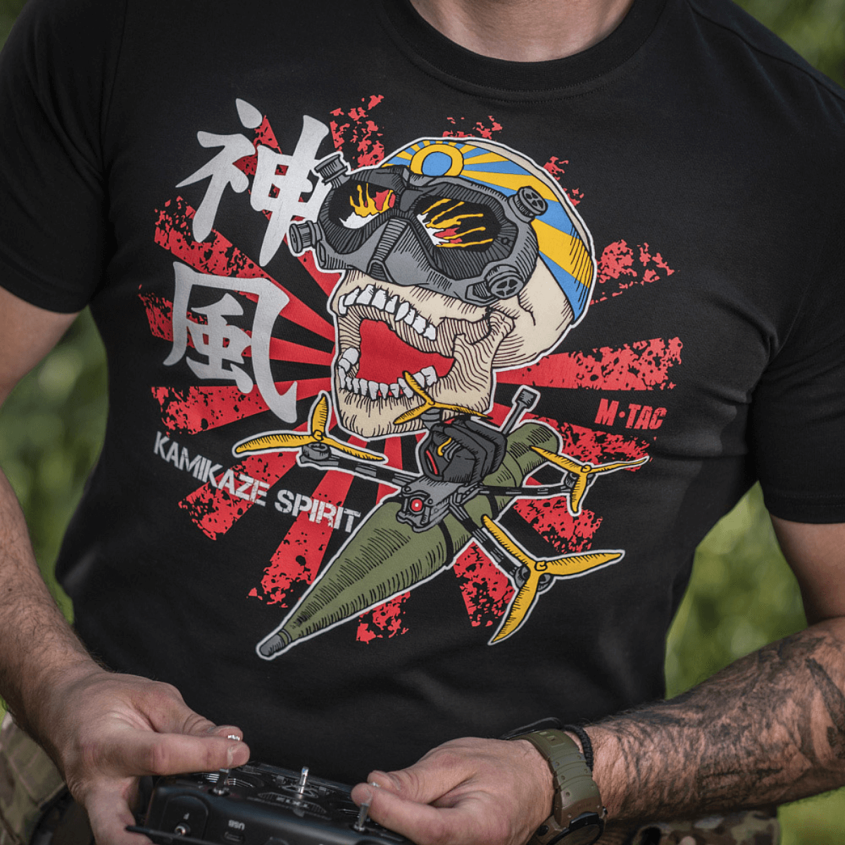 Mand iført M-Tac T-Shirt Kamikaze Spirit med stiliseret kranie og FPV-goggles på sort baggrund, japansk "Hinomaru" solflag baggrund.