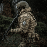 Soldat i camouflageuniform med M-Tac Patch M67 Granat 3D PVC på ærmet, bevæbnede i skoven.